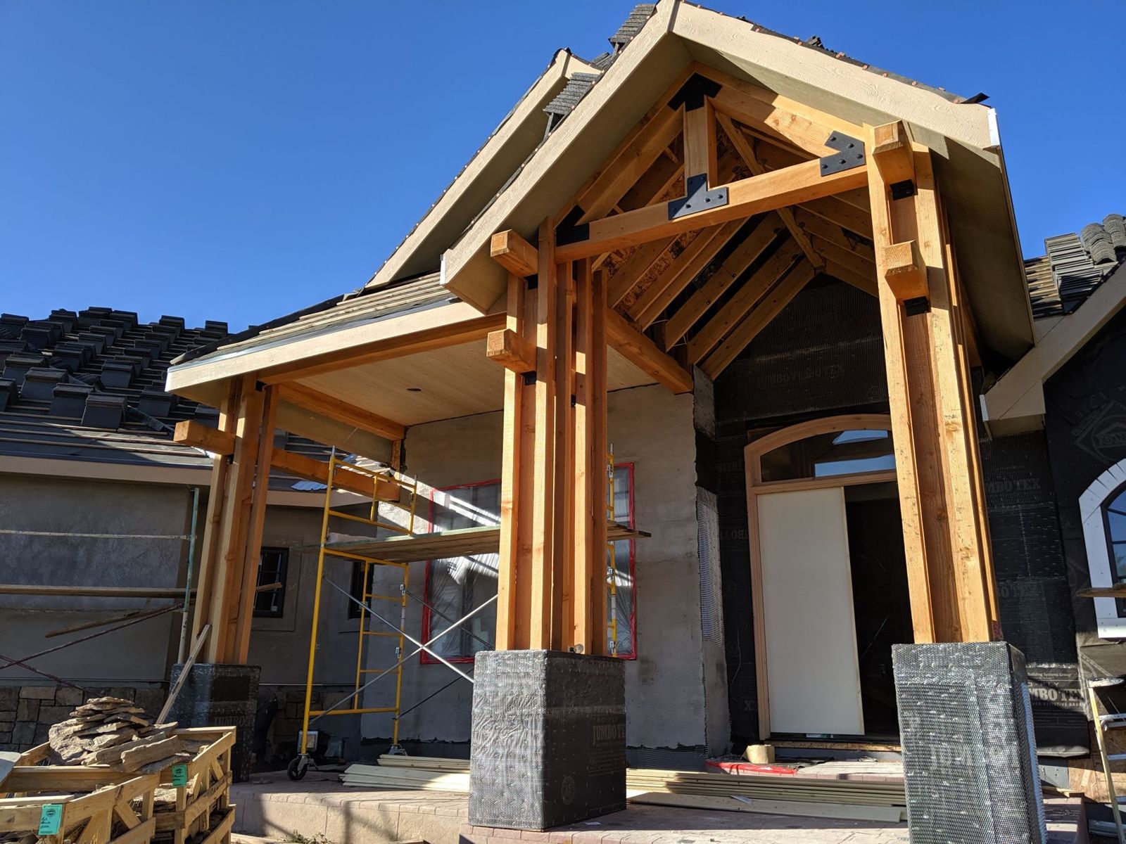 Heavy-timber entry with stone column bases on a two-story custom home under construction